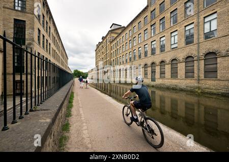 Un cycliste sur le chemin de halage du canal Leeds-Liverpool à Saltaire Mill, un site du patrimoine mondial, West Yorkshire, Royaume-Uni Banque D'Images