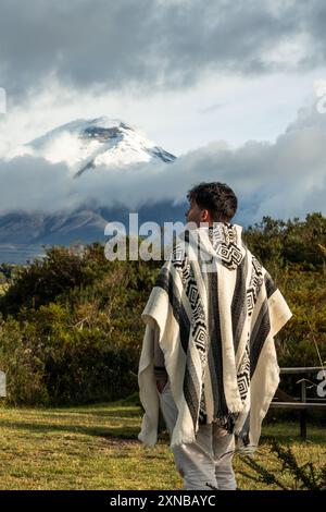 Jeune Latino portant un poncho traditionnel se tient devant le majestueux volcan Cotopaxi, qui culmine à 5 897 mètres, en Équateur. capture le culte Banque D'Images