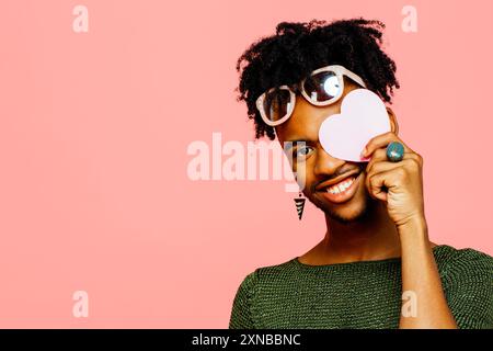 Portrait d'un jeune homme souriant tenant un cœur rose, isolé sur fond rose de studio Banque D'Images