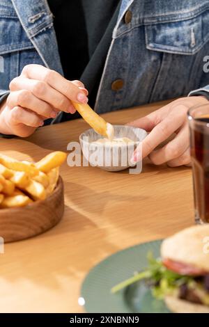 La femme déverse des frites dans la sauce à la table en bois Banque D'Images