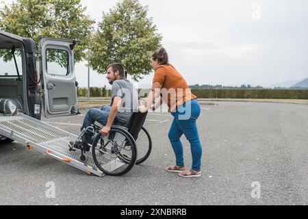 Assistante féminine aidant une personne masculine en fauteuil roulant avec le transport en utilisant la rampe de fourgonnette de véhicule accessible. Handicap et concepts de mobilité. Banque D'Images