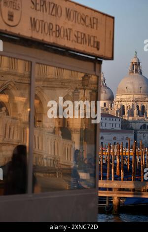 Venise, Italie, dômes de Santa Maria della Salute attrapant la lumière du soleil à l'aube et reflets du Palais des Doges dans le guichet du service de taxi à Molo Banque D'Images