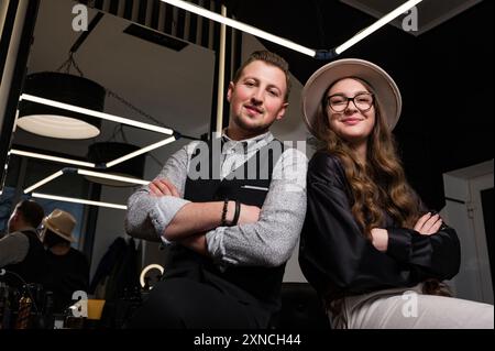Un couple de barbiers se regardent assis sur une chaise dans un intérieur moderne d'un salon de coiffure. Banque D'Images