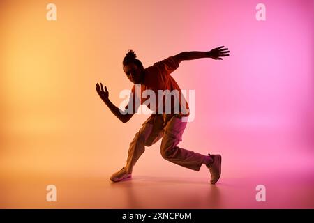 Un jeune danseur afro-américain effectue un mouvement de danse hip-hop sur un fond coloré dégradé dans un studio. Banque D'Images