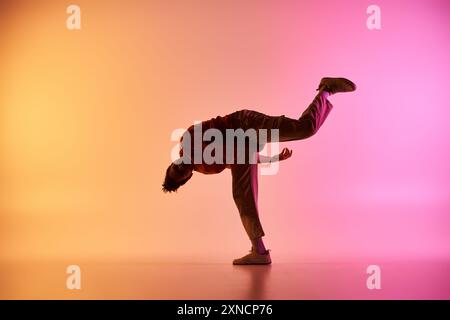 Un jeune danseur afro-américain effectue une pose dynamique sur un fond dégradé coloré. Banque D'Images