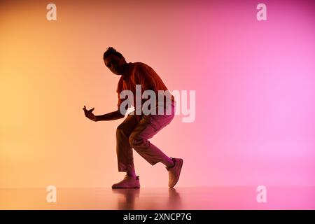 Un jeune danseur afro-américain effectue un mouvement sur un fond dégradé coloré. Banque D'Images