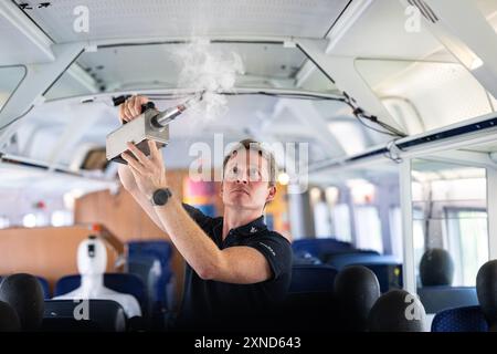 Minden, Allemagne. 31 juillet 2024. Daniel Schmeling, du Centre aérospatial allemand (DLR), pulvérise de la fumée dans le compartiment du train avec une machine à fumée dans un wagon d'essai de la Deutsche Bahn pour tester la turbulence de l'air pour les passagers. Le Centre aérospatial allemand (DLR) de Göttingen mène des recherches sur les systèmes de climatisation des trains dans un wagon d'essai Deutsche Bahn. Crédit : Guido Kirchner/dpa/Alamy Live News Banque D'Images