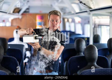 Minden, Allemagne. 31 juillet 2024. Daniel Schmeling, du Centre aérospatial allemand (DLR), pulvérise de la fumée dans le compartiment du train avec une machine à fumée dans un wagon d'essai de la Deutsche Bahn pour tester la turbulence de l'air pour les passagers. Le Centre aérospatial allemand (DLR) de Göttingen mène des recherches sur les systèmes de climatisation des trains dans un wagon d'essai Deutsche Bahn. Crédit : Guido Kirchner/dpa/Alamy Live News Banque D'Images