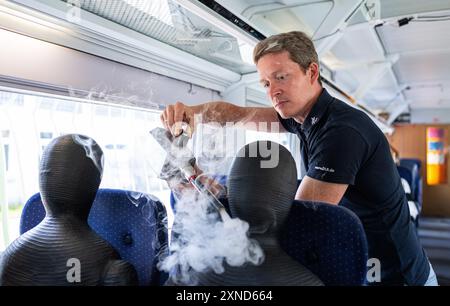 Minden, Allemagne. 31 juillet 2024. Daniel Schmeling, du Centre aérospatial allemand (DLR), pulvérise de la fumée sur un mannequin dans un chariot d'essai de la Deutsche Bahn à l'aide d'une machine à fumée pour tester les turbulences de l'air subies par les passagers. Le Centre aérospatial allemand (DLR) de Göttingen mène des recherches sur les systèmes de climatisation des trains dans un wagon d'essai Deutsche Bahn. Crédit : Guido Kirchner/dpa/Alamy Live News Banque D'Images