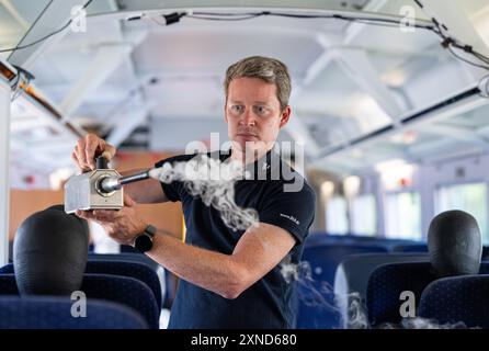 Minden, Allemagne. 31 juillet 2024. Daniel Schmeling, du Centre aérospatial allemand (DLR), pulvérise de la fumée dans le compartiment du train avec une machine à fumée dans un wagon d'essai de la Deutsche Bahn pour tester la turbulence de l'air pour les passagers. Le Centre aérospatial allemand (DLR) de Göttingen mène des recherches sur les systèmes de climatisation des trains dans un wagon d'essai Deutsche Bahn. Crédit : Guido Kirchner/dpa/Alamy Live News Banque D'Images