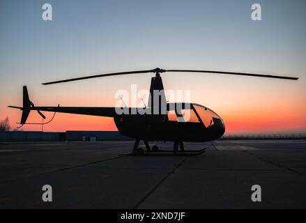 Silhouette d'hélicoptère contre un coucher de soleil vibrant sur la piste d'atterrissage de l'aéroport Banque D'Images