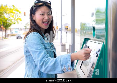 Jeune femme souriante achetant un billet pour les transports en commun à la machine automatique. Banque D'Images