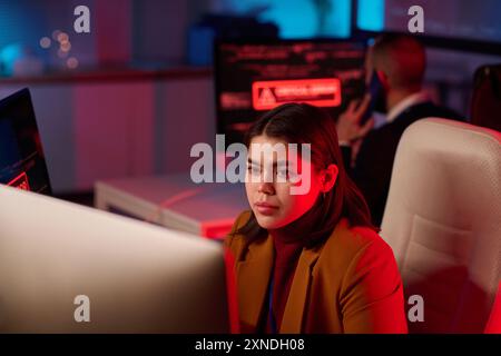 Portrait d'une jeune femme utilisant un ordinateur dans le département de cybersécurité éclairé par un espace de copie de lumière de néon rouge Banque D'Images