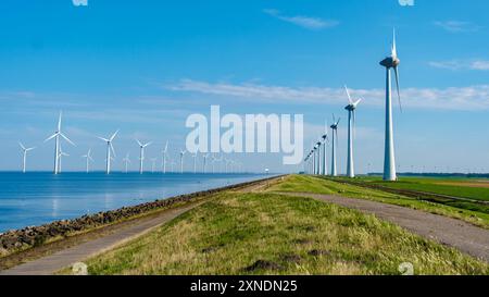 Les éoliennes sont hautes le long de la paisible côte néerlandaise des digues, exploitant l'énergie éolienne pour promouvoir la durabilité dans un contexte de ciel clair et d'eaux bleues aux pays-Bas Banque D'Images