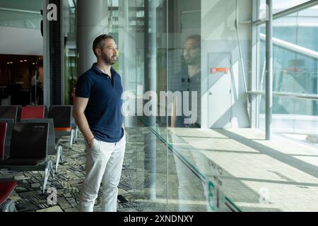 Homme debout contre la fenêtre dans la salle d'attente de l'aéroport Banque D'Images