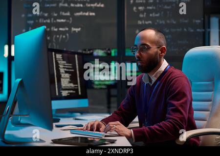 Portrait de vue de côté d'un homme adulte portant des lunettes et écrivant du code à l'aide d'un ordinateur dans le département de cybersécurité moderne avec des murs de verre espace de copie Banque D'Images