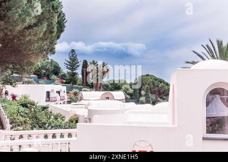 Un hôtel méditerranéen pittoresque entouré de verdure luxuriante et de palmiers sous un ciel nuageux. Banque D'Images