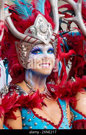 Cette image capture un portrait en gros plan d'une femme souriante regardant directement la caméra, ornée d'un costume vibrant et d'un maquillage coloré. Banque D'Images