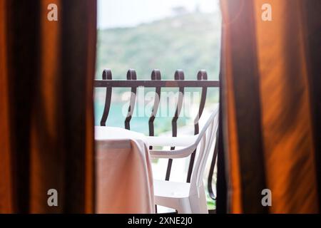 Une vue de derrière les rideaux montrant un balcon d'hôtel avec un paysage pittoresque de verdure et d'océan en Italie. Banque D'Images