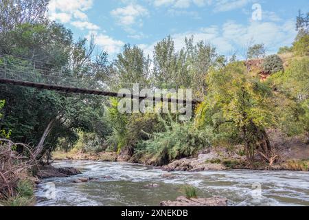 Vue d'un sentier de randonnée Hennops, avec rivière qui traverse, petit pont et téléphérique au-dessus de la rivière, Hartbeespoort, Johannesburg, Afrique du Sud Banque D'Images