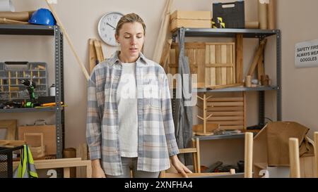Une jeune femme pensive se tient dans un atelier de menuiserie bien équipé, entourée d'outils de travail du bois. Banque D'Images
