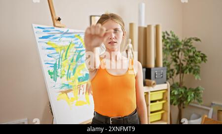 Une jeune femme artiste concentrée dans un studio observe sa peinture colorée, mettant en valeur l'expression créative et la passion artistique. Banque D'Images