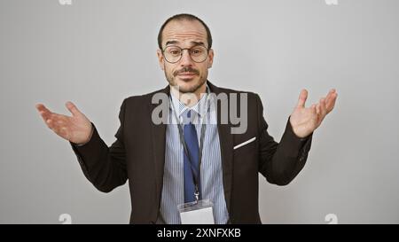 Un homme chauve et barbu en costume fait des gestes incertains sur un fond blanc, portant des lunettes et une longe. Banque D'Images