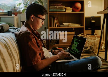 Étudiant assis sur le sol en position lotus tout en écrivant des codes pour son application personnelle Banque D'Images