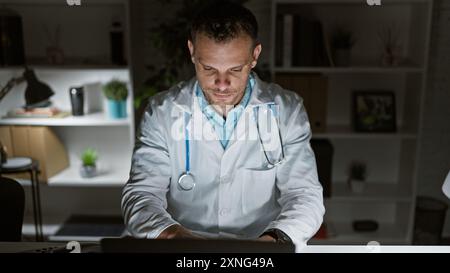 Concentré jeune professionnel de la santé travaillant sur ordinateur dans le bureau de la clinique la nuit. Banque D'Images