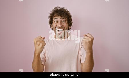 Un jeune homme hispanique joyeux célèbre avec les poings pompés sur un fond rose Uni. Banque D'Images
