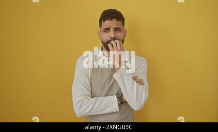 Un jeune homme hispanique réfléchi avec une barbe se tient sur un fond jaune solide, semblant pensif. Banque D'Images