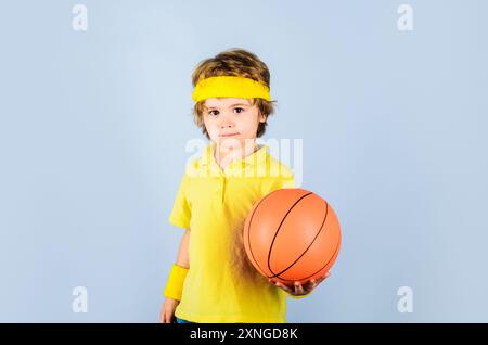 Petit basket-ball en vêtements de sport avec ballon de basket-ball. Sport pour enfants. Garçon souriant en uniforme de sport avec balle. Enfant sportif avec ballon de basket-ball Banque D'Images