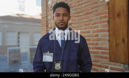 Portrait d'un homme afro-américain confiant en uniforme de police avec badge et ID debout à l'extérieur dans une ville. Banque D'Images