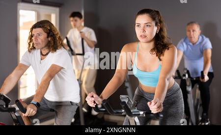 Homme et femme prenant un cours de vélo intérieur au centre de fitness, faisant du vélo cardio-porté Banque D'Images