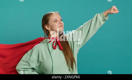 Portrait de Jolly girl portant un costume de super-héros pour Halloween, isolé sur fond de studio. Adolescent radieux habillé en héros de bande dessinée pour l'événement, montrant courage et force, caméra A. Banque D'Images