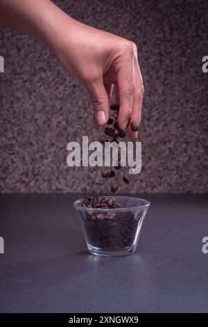 Mains féminines contenant des grains de café frais, les grains de café tombent dans un récipient en verre sur un fond en bois, espace de copie Banque D'Images