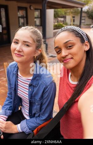 Des adolescentes souriantes assises ensemble devant le lycée, profitant de leur pause Banque D'Images