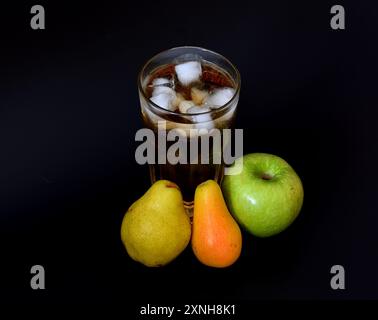 Jus de pomme et de poire dans un grand verre à facettes avec de la glace sur un fond noir, à côté de fruits mûrs. Gros plan. Banque D'Images