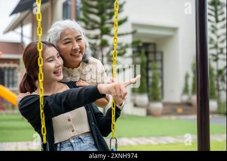 Une heureuse petite-fille asiatique est sur une balançoire, profitant d'une conversation avec sa grand-mère dans leur arrière-cour. moment heureux, liens familiaux, ensemble Banque D'Images