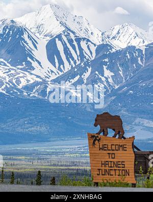 Vue printanière de Haines Junction dans la région du nord du Canada avec panneau de bienvenue avec un ours et un énorme fond de montagnes enneigées Banque D'Images