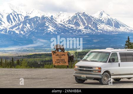 Vue printanière de Haines Junction dans la région du nord du Canada avec panneau de bienvenue avec un ours et un énorme fond de montagnes enneigées Banque D'Images