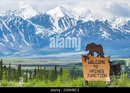 Vue printanière de Haines Junction dans la région du nord du Canada avec panneau de bienvenue avec un ours et un énorme fond de montagnes enneigées Banque D'Images