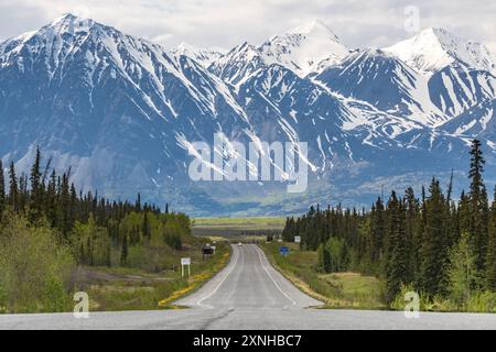 Route de l'Alaska en voiture dans la ville de Haines Junction au printemps avec des montagnes énormes et épiques à distance avec une incroyable route panoramique en avant. Banque D'Images