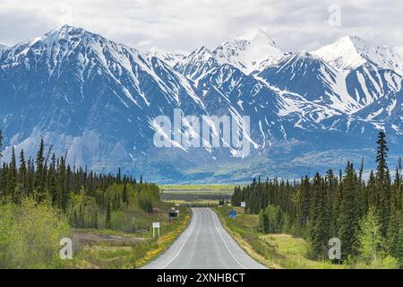 Route de l'Alaska en voiture dans la ville de Haines Junction au printemps avec des montagnes énormes et épiques à distance avec une incroyable route panoramique en avant. Banque D'Images