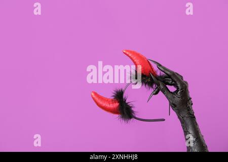 Main de sorcière avec bandeau rouge de cornes de diable sur fond violet. Célébration d'Halloween Banque D'Images