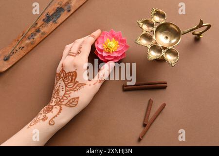 Main féminine avec lampe diya, bâton d'encens, cannelle et fleur de lotus pour la célébration de Divaly sur fond brun Banque D'Images