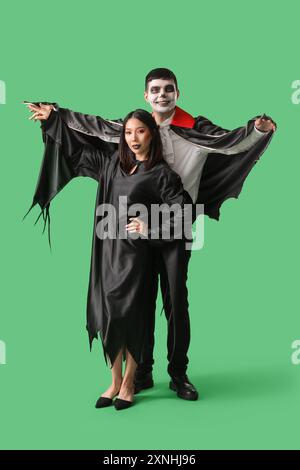 Jeune couple en costumes pour la fête d'Halloween sur fond vert Banque D'Images