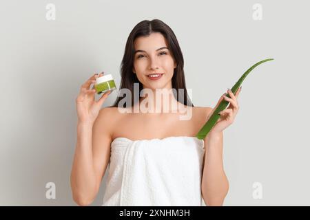 Belle jeune femme heureuse avec feuille de plante et pot de gel d'aloe vera sur fond gris Banque D'Images