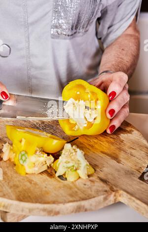 Gros plan de mains coupant un poivron jaune sur une planche à découper en bois, présentant la préparation de cuisson et les ingrédients frais. Banque D'Images