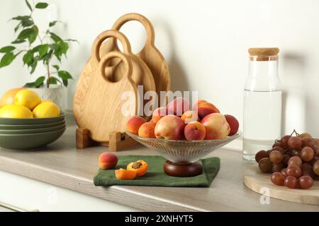 Vase en verre avec différents fruits frais, bouteille et ensemble de planches à découper sur le comptoir en bois dans la cuisine Banque D'Images